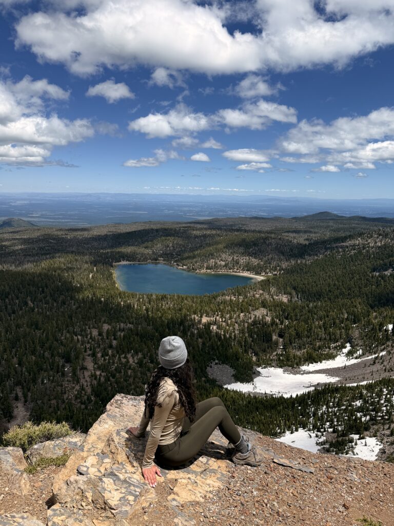 woman sitting alone on mountain summit overlooking alpine lake, solo travel photo taken with phone tripod