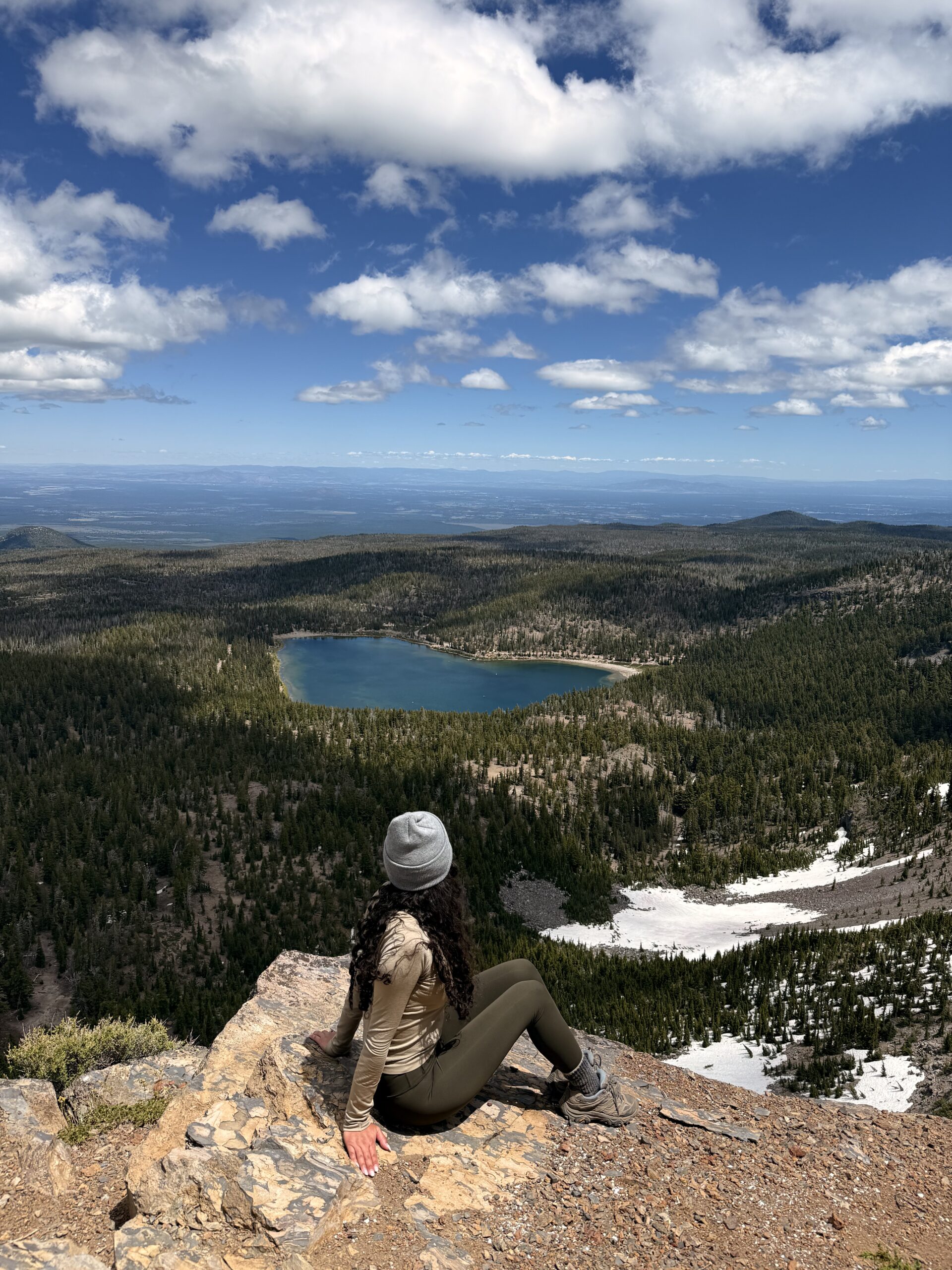 woman sitting alone on mountain summit overlooking alpine lake, solo travel photo taken with phone tripod