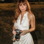 Woman holding a camera in a sunlit field during golden hour