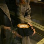 Woman holding an aesthetic latte at a cafe table with natural window light