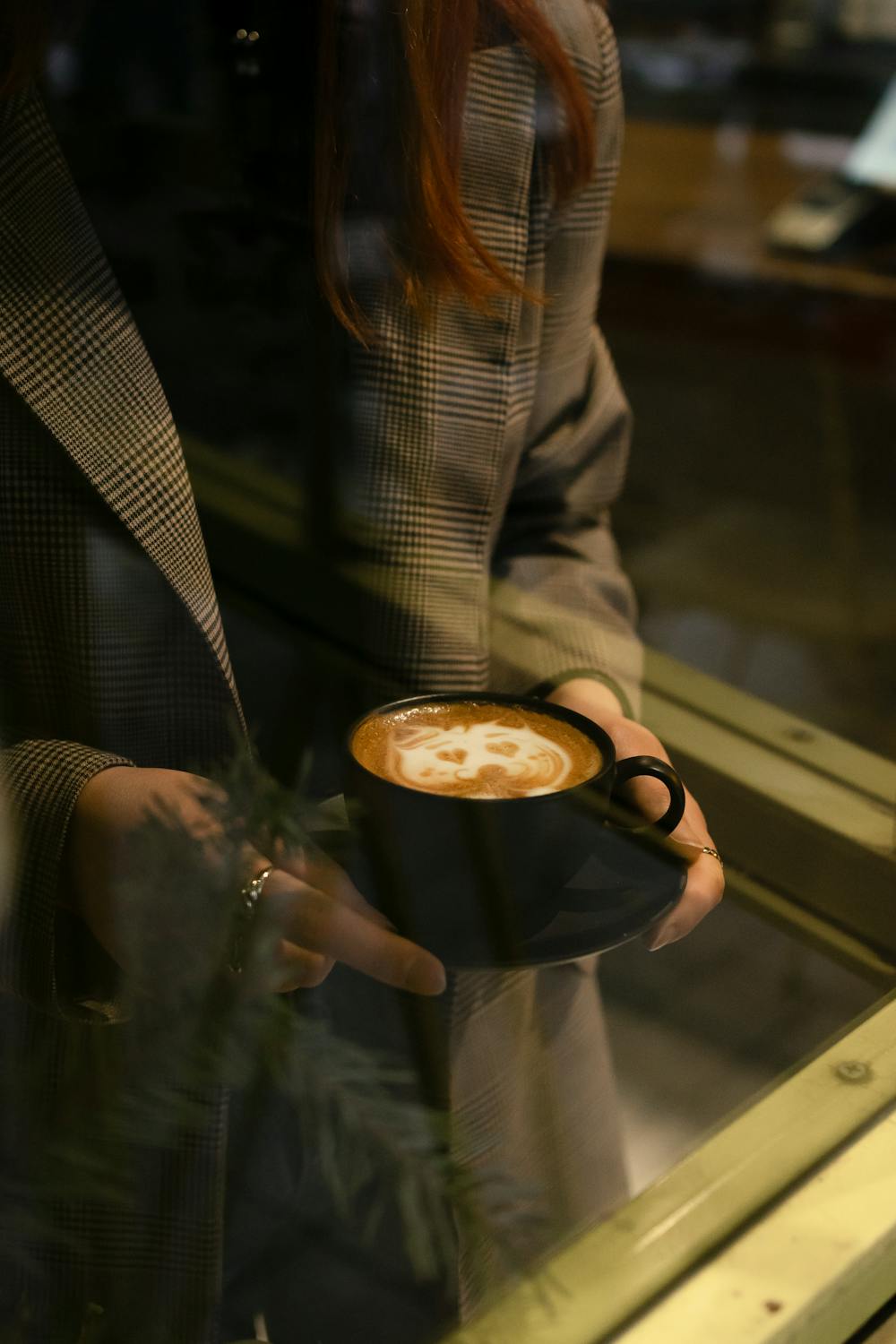Woman holding an aesthetic latte at a cafe table with natural window light