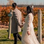 Couple walking through an autumn vineyard at a fall wedding, woman in elegant beige wedding guest outfit