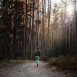 Woman walking along a sunlit autumn forest trail for fall photoshoot ideas