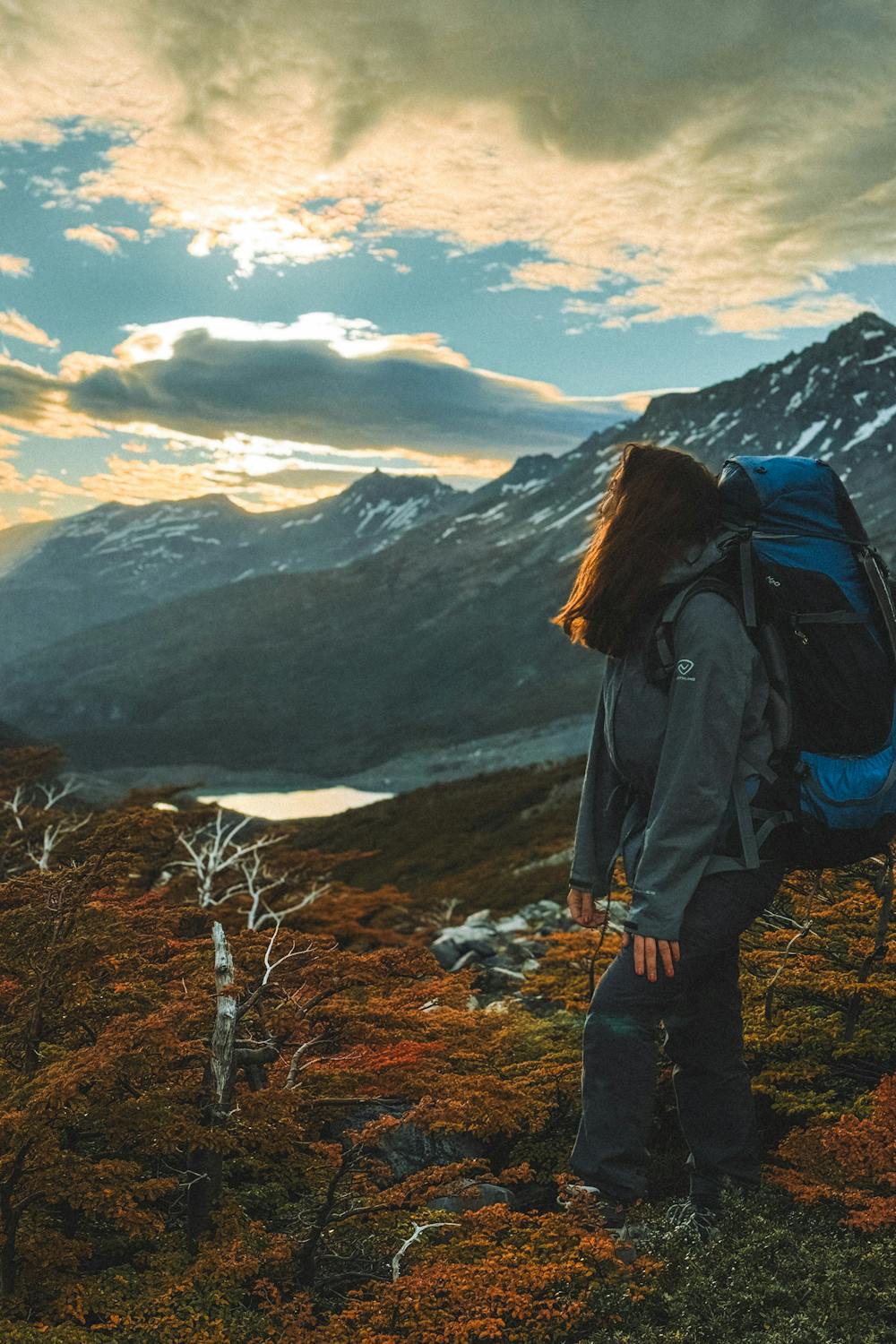 Woman with a hiking backpack standing at sunset on a mountain trail