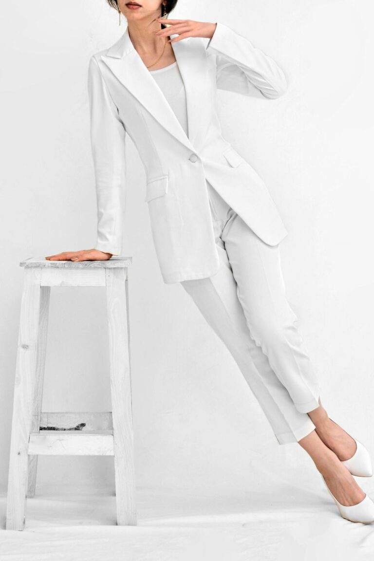 Woman in a clean white minimalist outfit standing beside a white stool