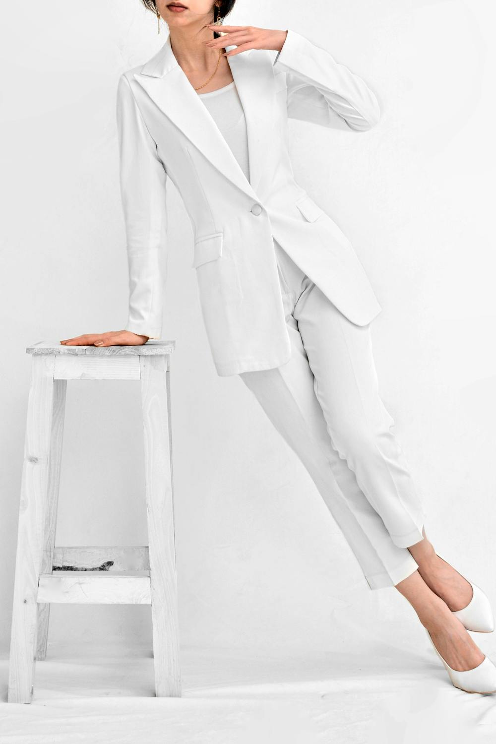 Woman in a clean white minimalist outfit standing beside a white stool