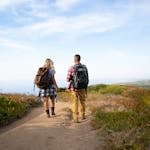 Couple walking a scenic coastal trail on a hiking date with ocean views and hillside vegetation