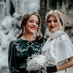 Two women at a winter wedding in elegant outfits — one in deep green velvet dress, one in ivory — ideal winter wedding guest outfit colors