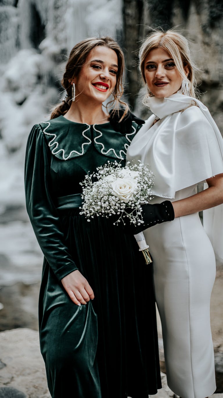 Two women at a winter wedding in elegant outfits — one in deep green velvet dress, one in ivory — ideal winter wedding guest outfit colors