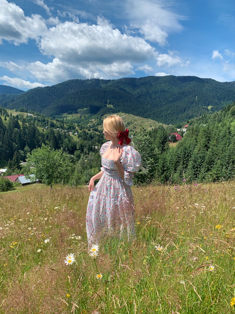 Woman in a whimsical cottagecore floral dress standing in a wildflower meadow with Carpathian mountains behind her