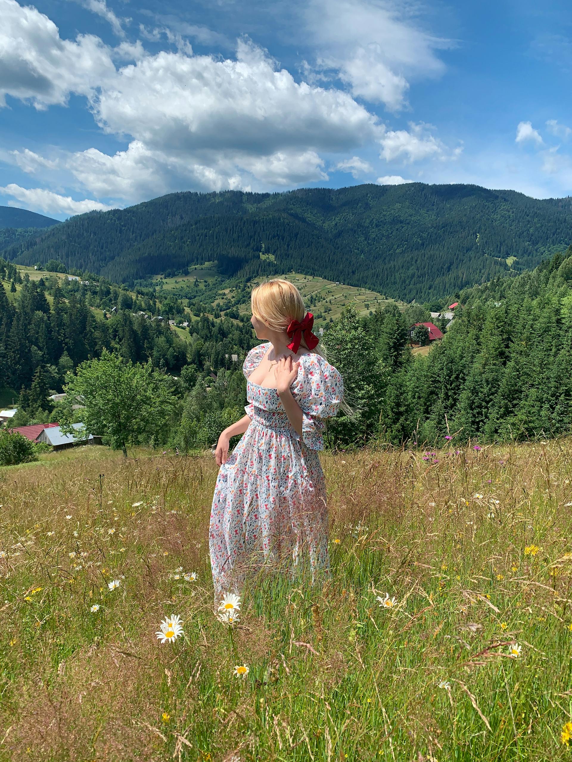 Woman in a whimsical cottagecore floral dress standing in a wildflower meadow with Carpathian mountains behind her