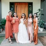 Women in terracotta and coral summer wedding guest outfits posing together outdoors at a summer wedding