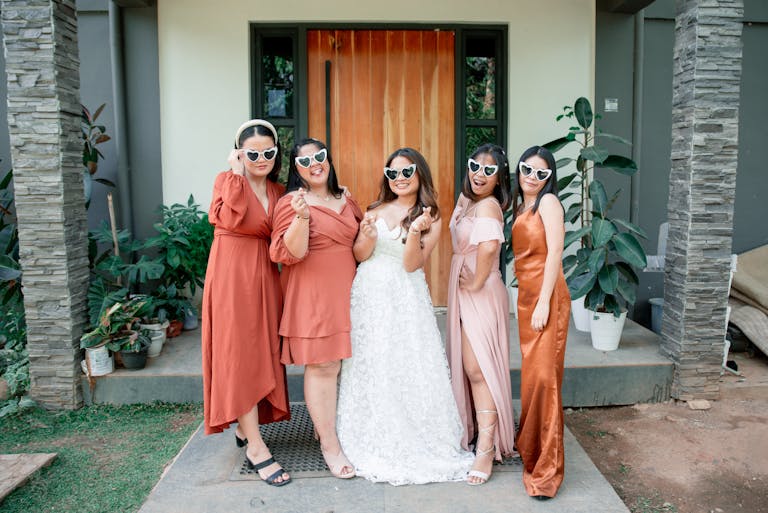 Women in terracotta and coral summer wedding guest outfits posing together outdoors at a summer wedding