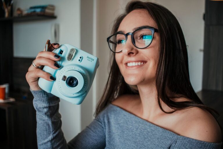 Woman smiling while holding a light blue Fujifilm Instax Mini camera — a perfect gift idea for the girlfriend who loves photos