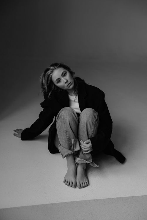 Woman in minimalist neutral outfit black coat and white shirt in clean studio setting