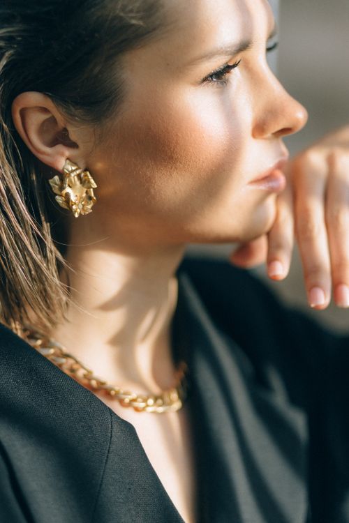 Woman wearing minimalist gold jewelry including a necklace and earrings in natural light
