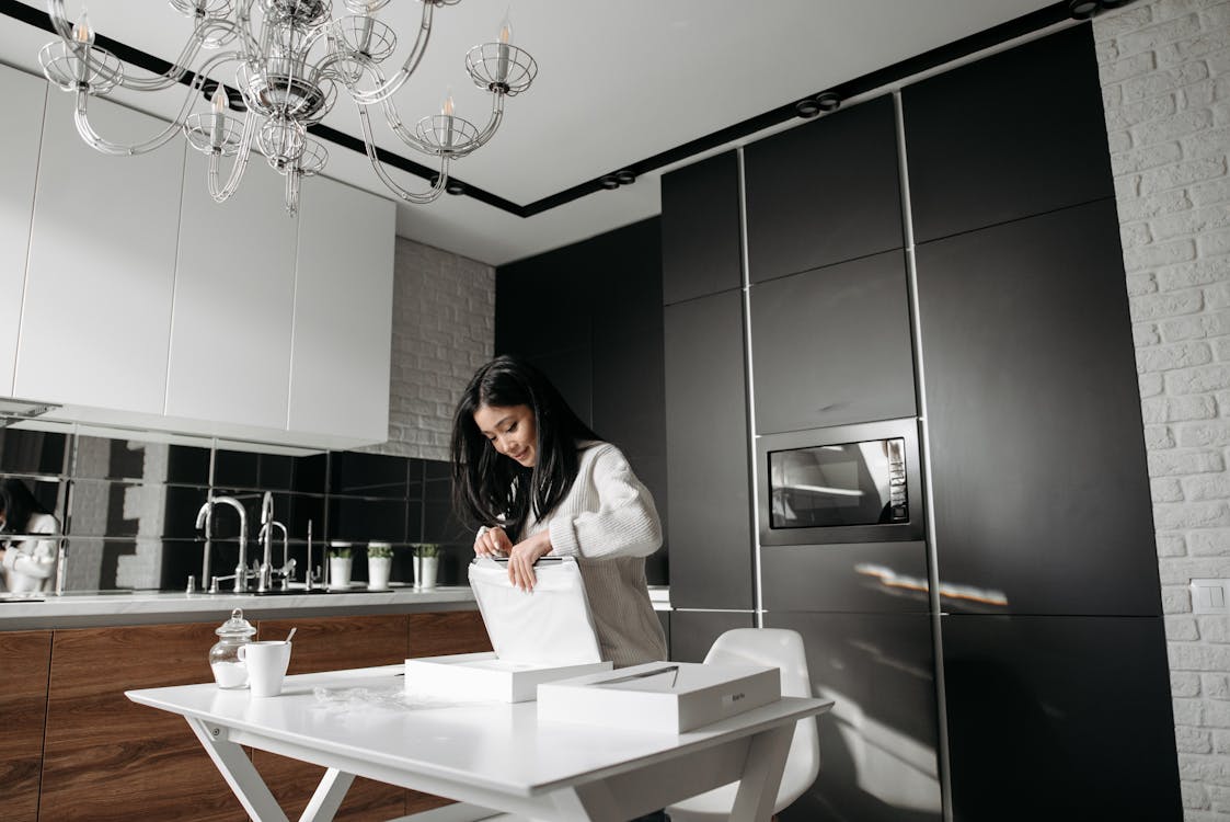 Woman in white sweater unboxing a package in her kitchen